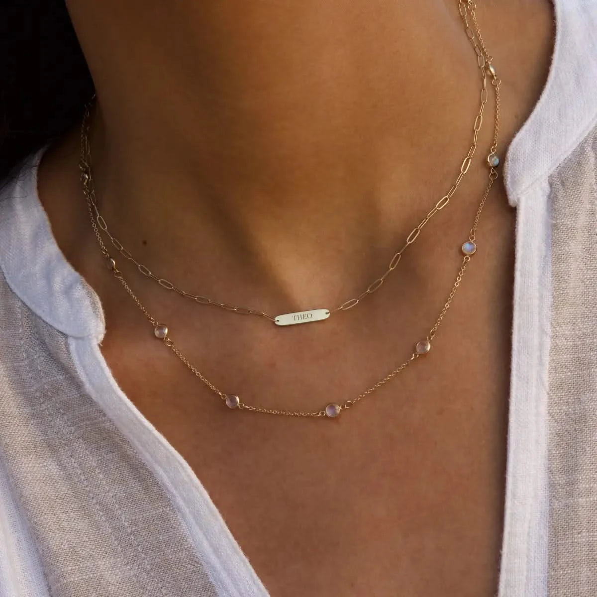 Close-up of woman wearing 1 Nameplate Necklace on Adelaide Mini paperclip chain, and Bayberry Moonstone Necklace in 14k yellow gold.