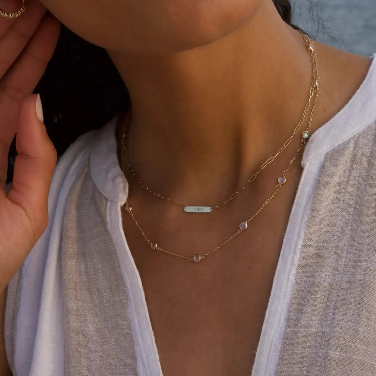 Detail shot of woman wearing 1 Nameplate Necklace on Adelaide Mini paperclip chain and Bayberry Moonstone Necklace in 14k yellow gold.