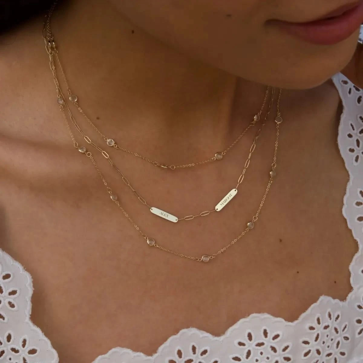Woman bwearing 2 Petite Nameplate Necklace on Adelaide Mini paperclip chain and Bayberry Moonstone Necklace, both in 14k yellow gold.