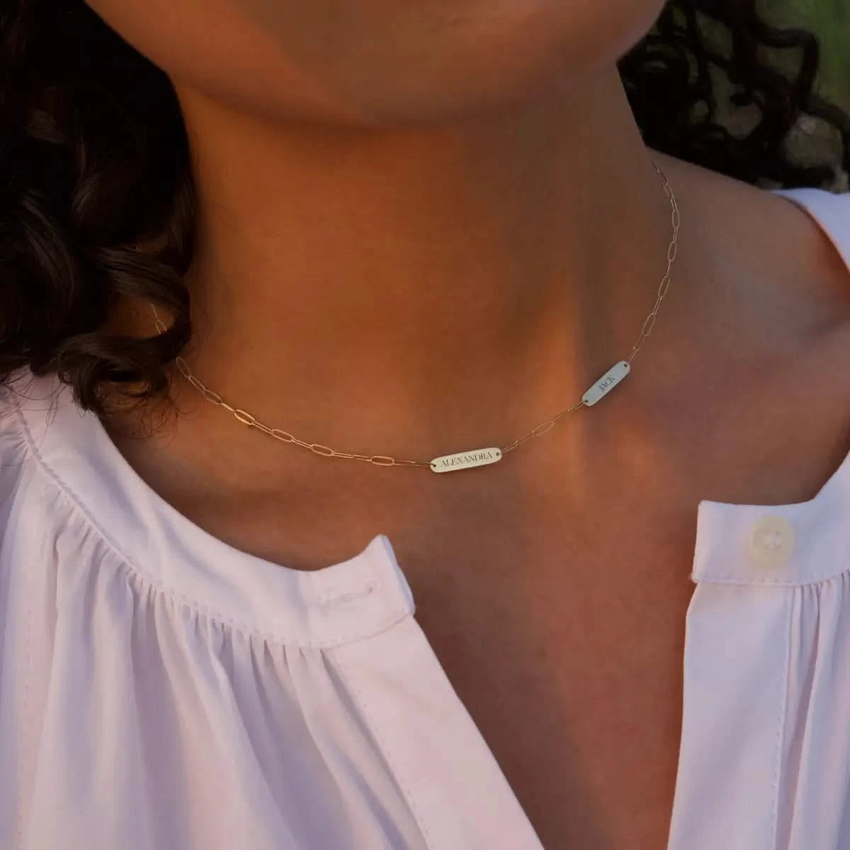 Close-up of woman in white blouse wearing 2 Petite Nameplate Necklace on Adelaide Mini chain in 14k gold, engraved with “ALEXANDRA” and “JACK”.