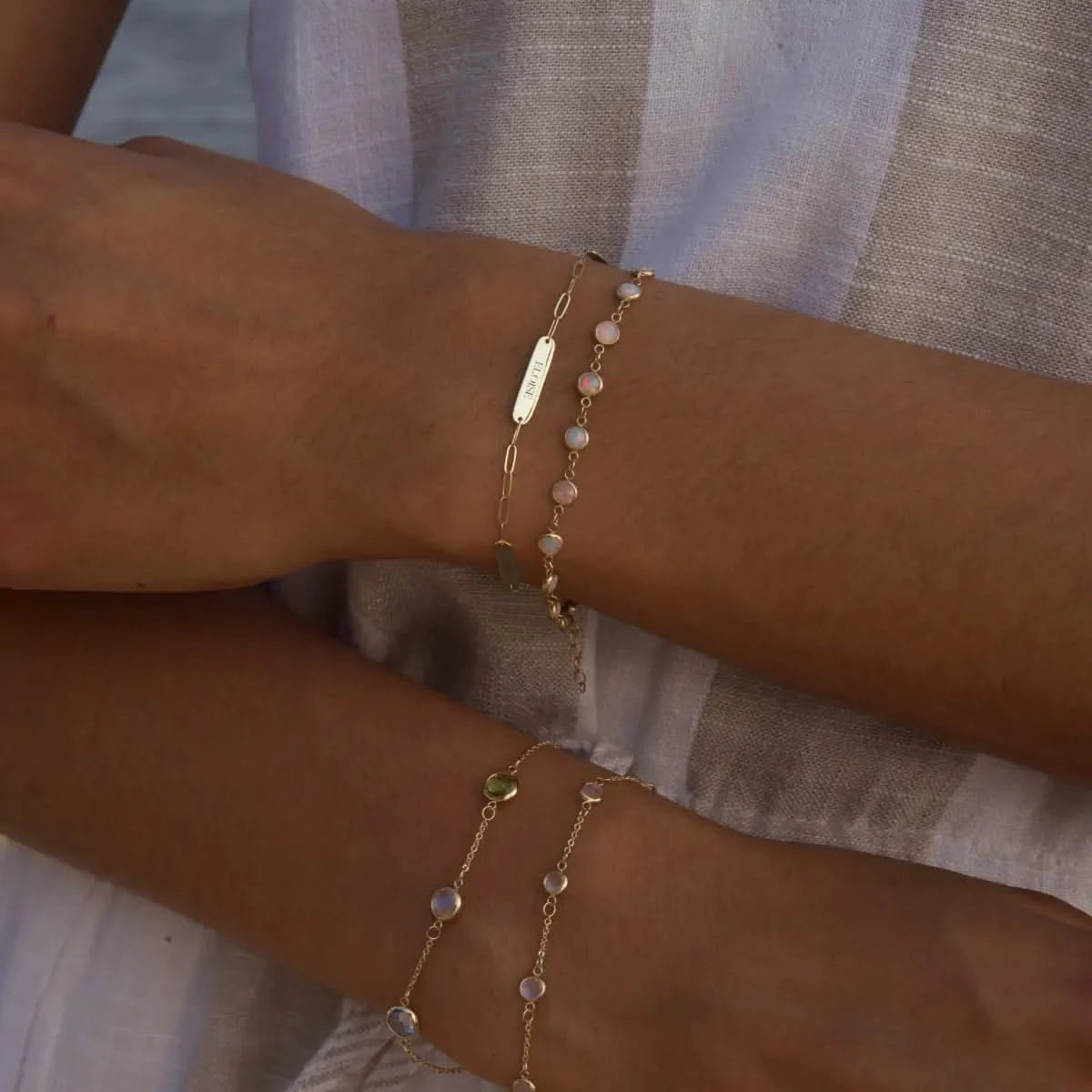 Woman near the ocean wearing 14k gold 3 Nameplate, Newport Opal, Bayberry Moonstone, and Grand Birthstone bracelets.