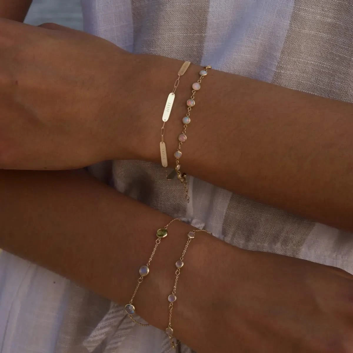 Woman near the ocean wearing 14k gold Nameplate, Newport Opal, Bayberry Moonstone, and Grand Birthstone bracelets.