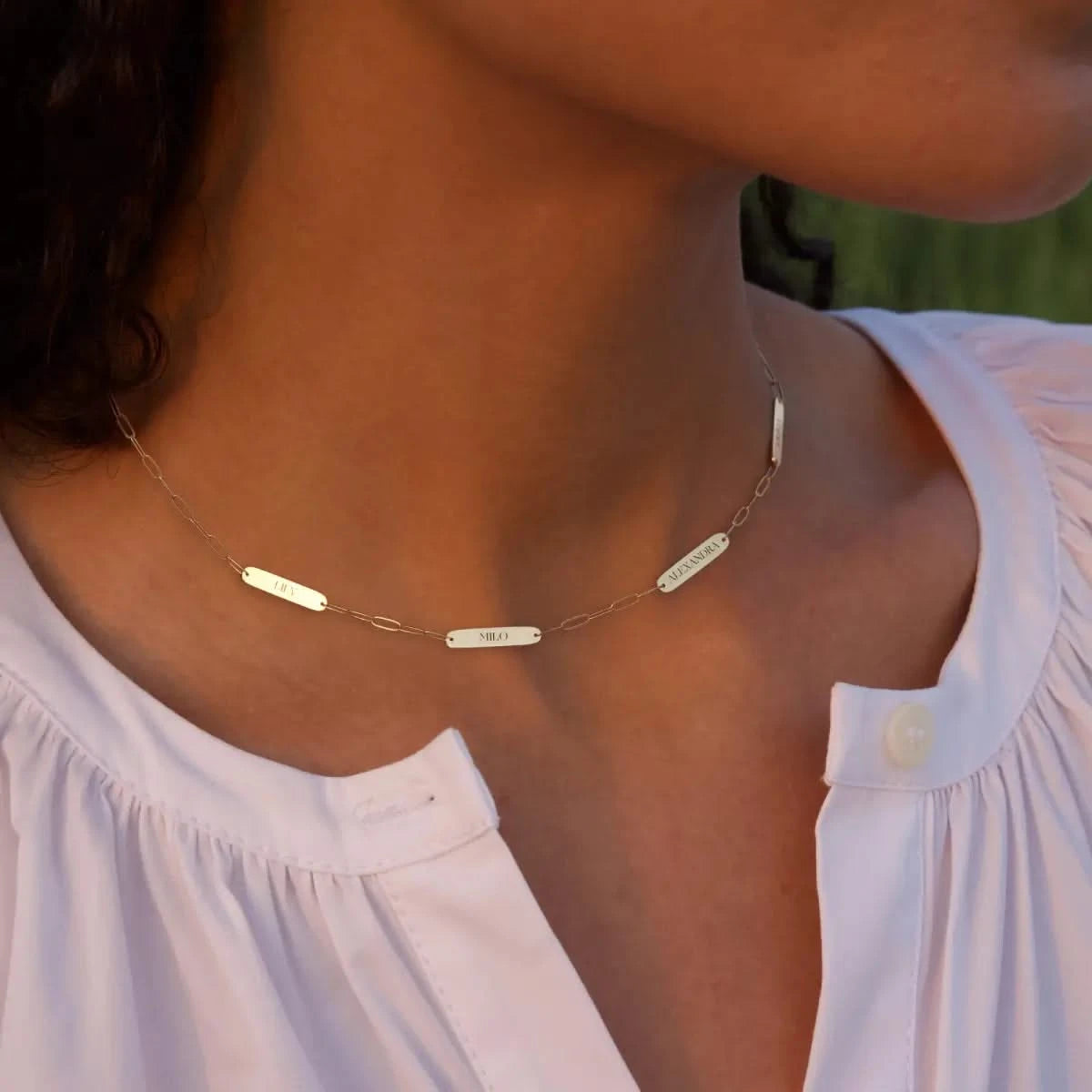Close-up of woman wearing 4 Petite Nameplate Necklace on Adelaide Mini paperclip chain in 14k gold engraved with her children’s names.