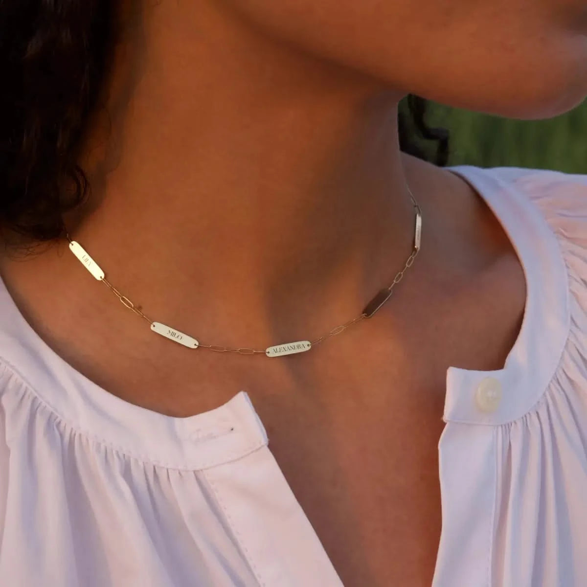 Close-up of woman wearing 5 Petite Nameplate Necklace on 14k gold Adelaide Mini paperclip chain, engraved with her children