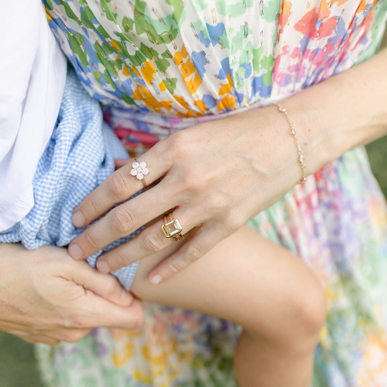 Woman wearing a bracelet and two rings including a Greenwich ring featuring five 4 mm faceted round cut opals and one 2.1 mm diamond prong set in 14k gold