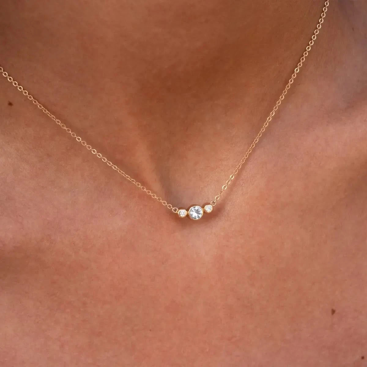 Close-up of Barrington 3 Stone Necklace featuring a 4 mm round cut White Topaz center stone framed by two 2 mm round cut Diamonds bezel set in 14k yellow gold on a saffron chain