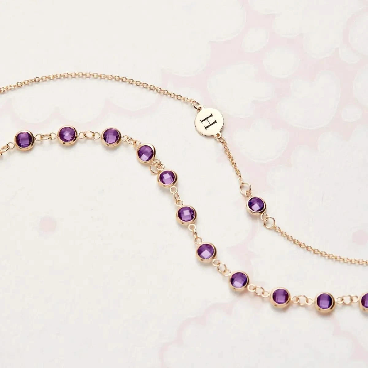 Flatlay of Newport Amethyst Bracelet in 14k gold featuring briolette cut Amethysts and engraved “H” charm near the clasp.