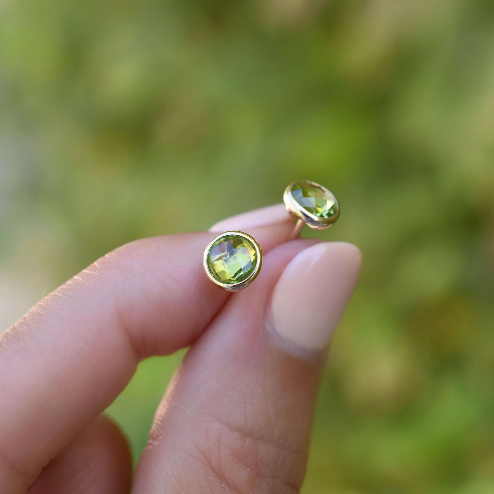 Woman showcasing a pair of 14k yellow gold Grand stud earrings each featuring one 6 mm briolette cut peridot