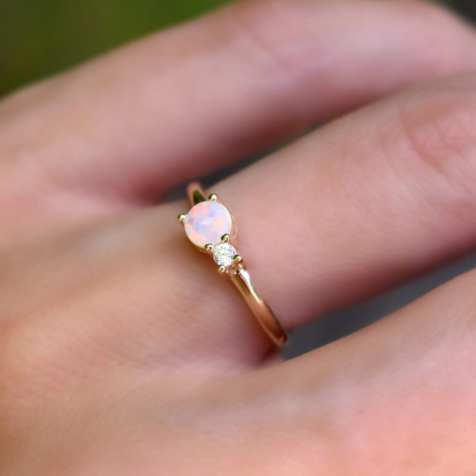 Hand wearing a Greenwich ring in 14k Yellow Gold featuring one 4 mm faceted round cut Solitaire Opal and one 2.1 mm diamond prong set