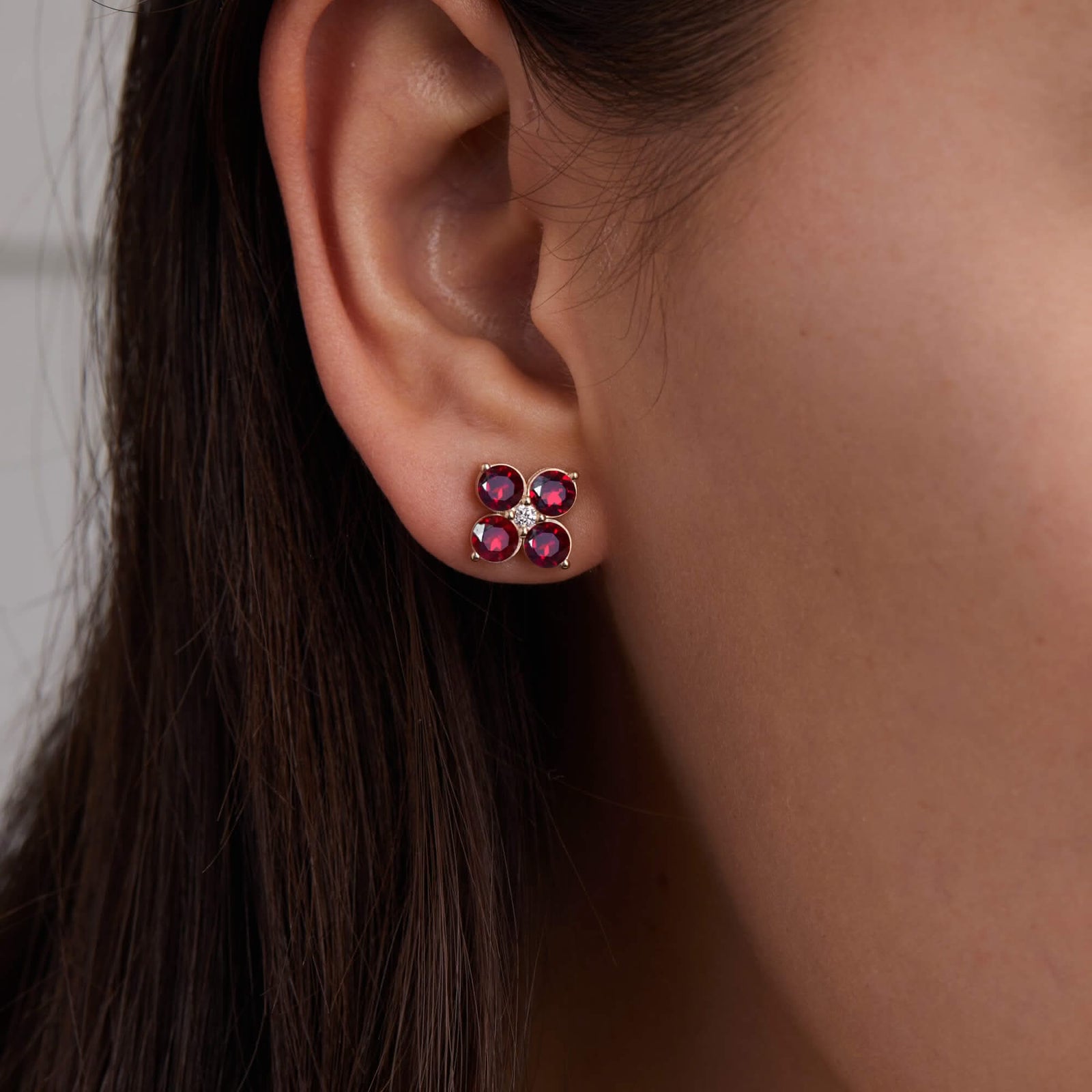 Woman showcasing a Greenwich Birthstone Earrings in 14k Gold featuring four 4 mm faceted round cut, prong set Rubies and one 2.1 mm Diamond.