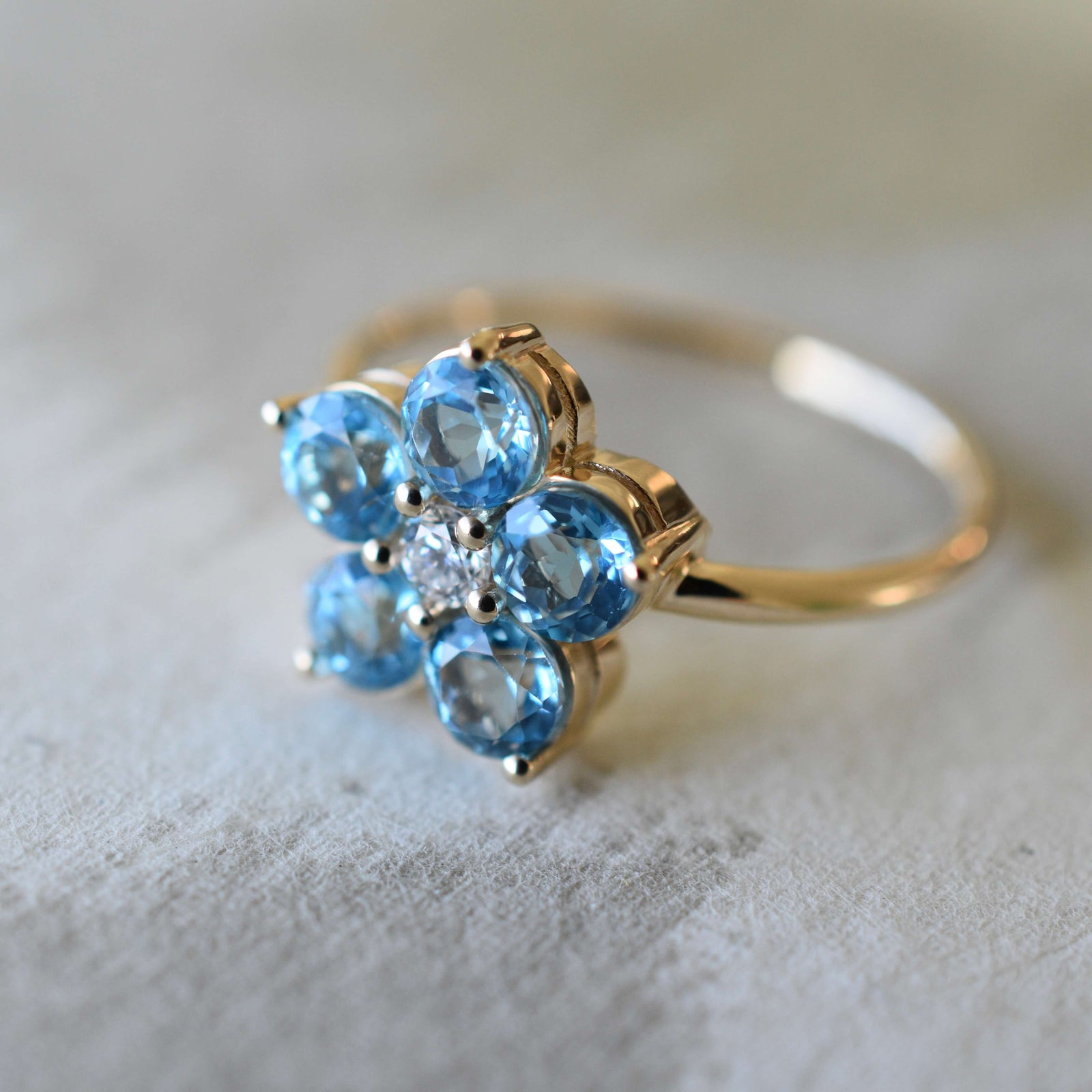 The Greenwich Nantucket Blue Topaz and Diamond Petal Ring showcases five brilliant Nantucket Blue Topaz stones prong set in 14k gold, surrounding an accent diamond.