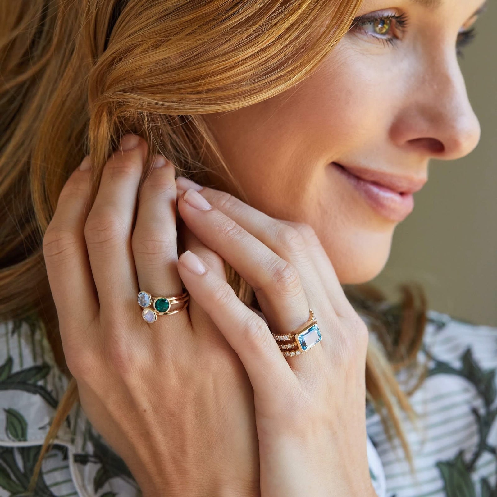 Woman wearing a personalized Grand Birthstone Rings with a 6mm round briolette-cut gemstone, a Rosecliff Diamond Stackable Ring perfect for February birthdays, and a Warren Horizontal Ring with diamonds and a stunning aquamarine bezel-cut.