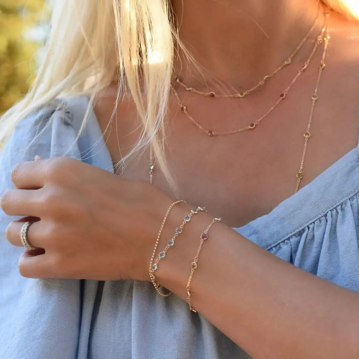 Woman wears layered gemstone bracelets and necklaces, including a Petite Newport Aquamarine Bracelet.