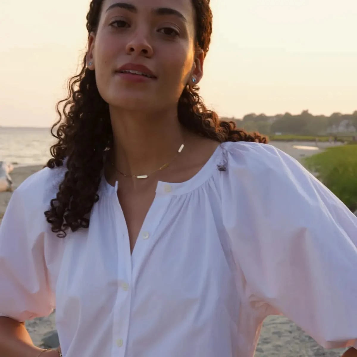 Woman at the beach wearing 5 Petite Nameplate Necklace on Adelaide Mini paperclip chain in 14k gold, styled with a white blouse.