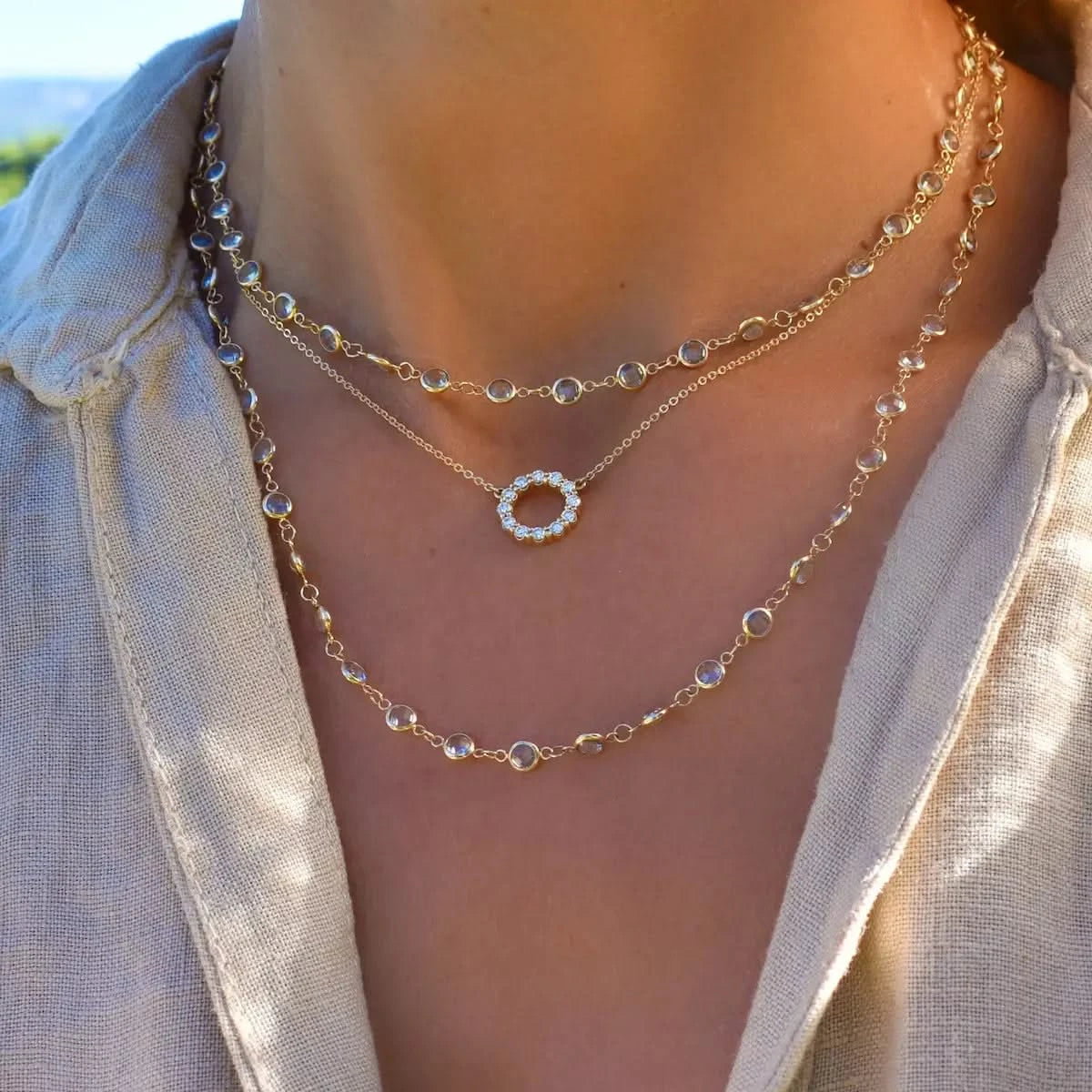 A woman wearing two layers of the Newport Aquamarine Long Necklace, paired with the Small Circle Diamond Necklace in 14k gold, elegantly wrapped around her neck.