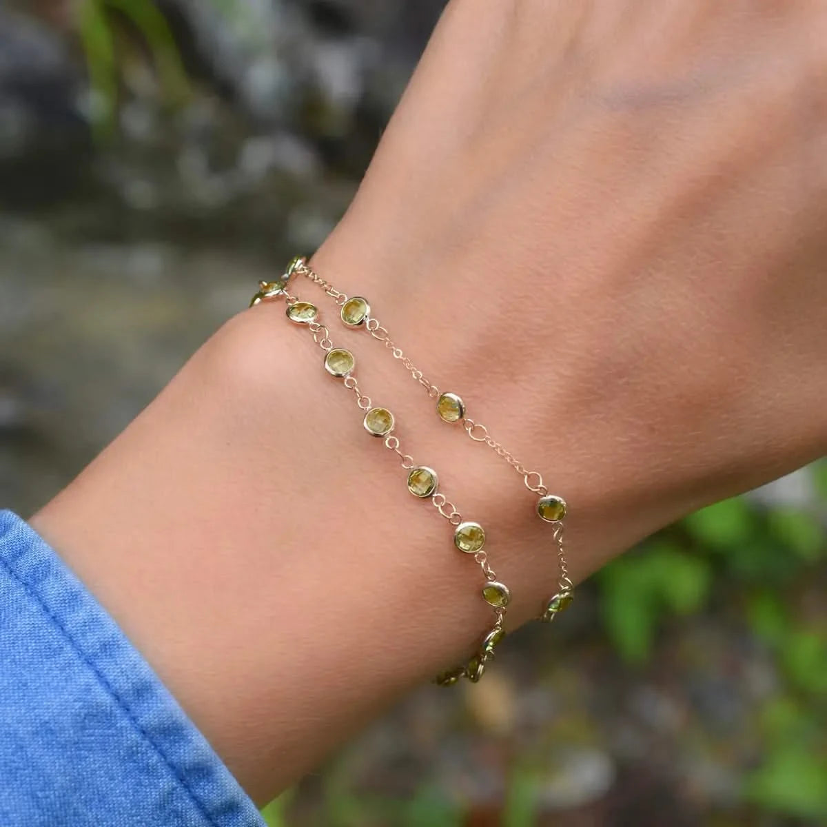 Woman wearing two bracelets including a Newport 14k yellow gold bracelet featuring 4 mm briolette cut bezel set peridots