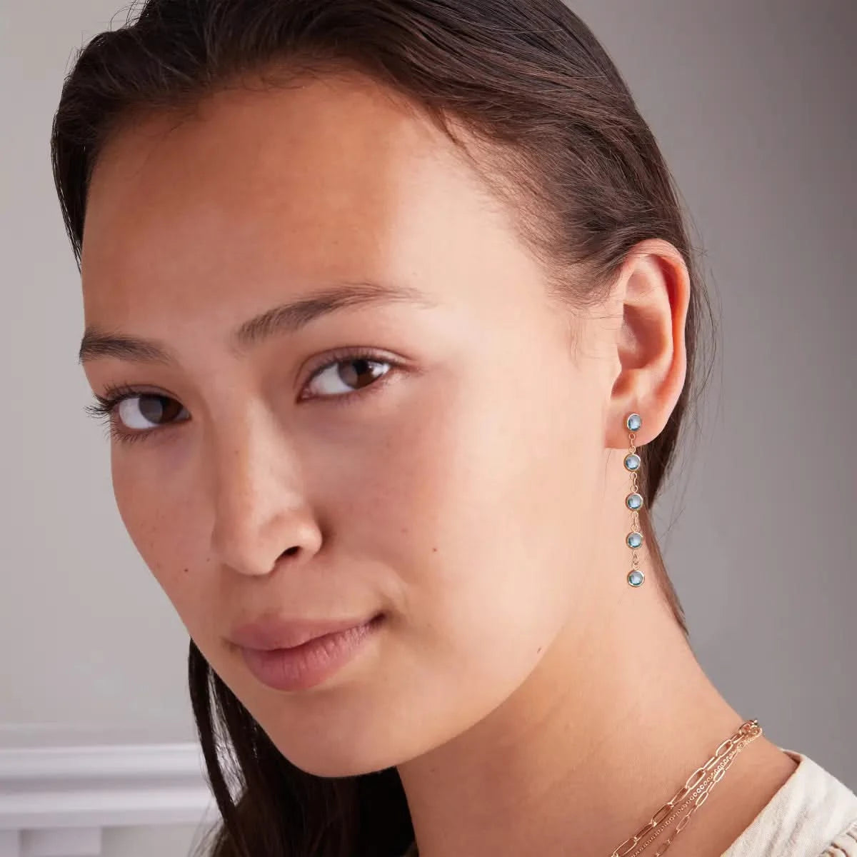 Woman wearing Newport Blue Topaz Earrings in 14k gold, highlighting their elegant dangle design with faceted gemstones.