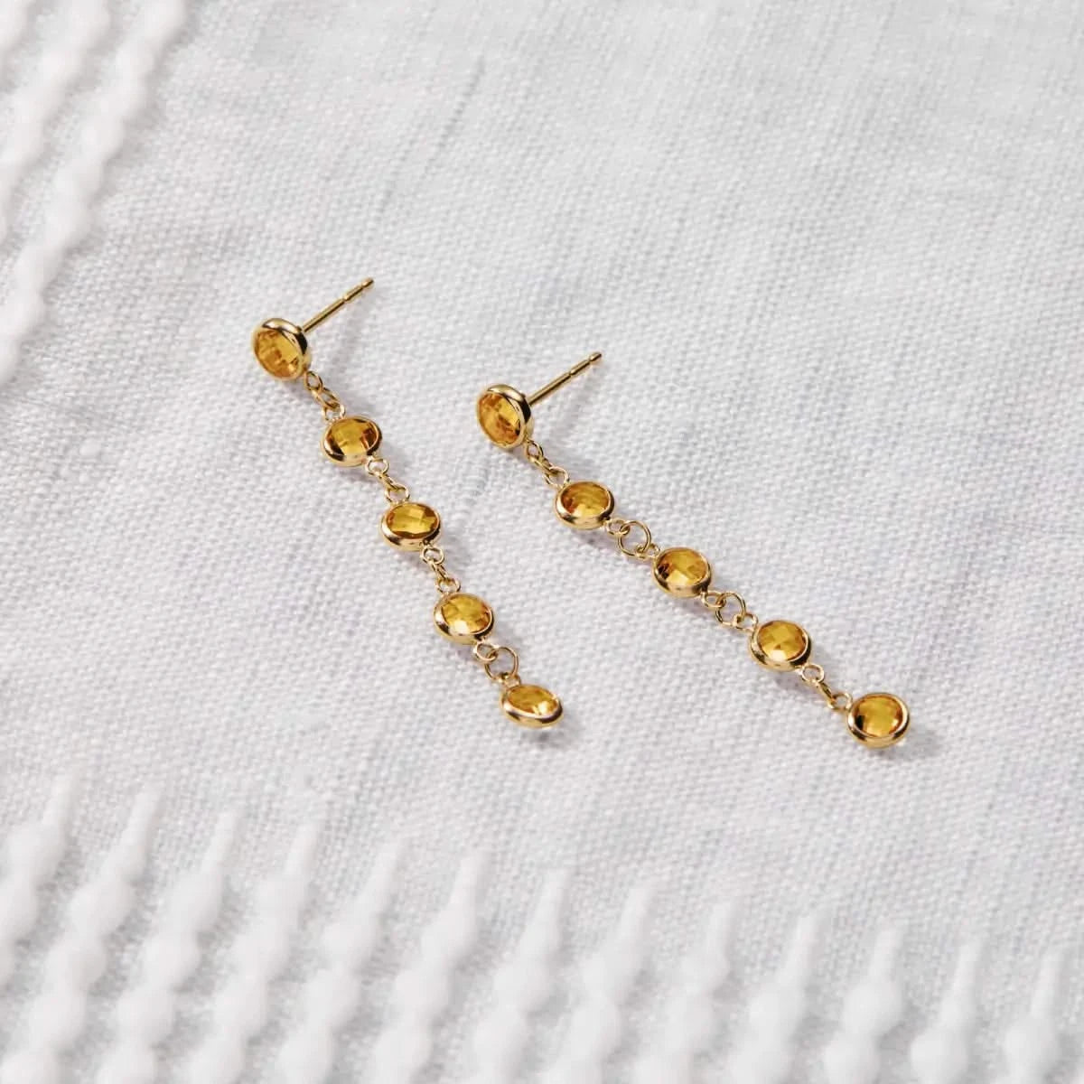 Newport Citrine Earrings in 14k gold are displayed on fabric, featuring five bezel-set briolette-cut Citrines.