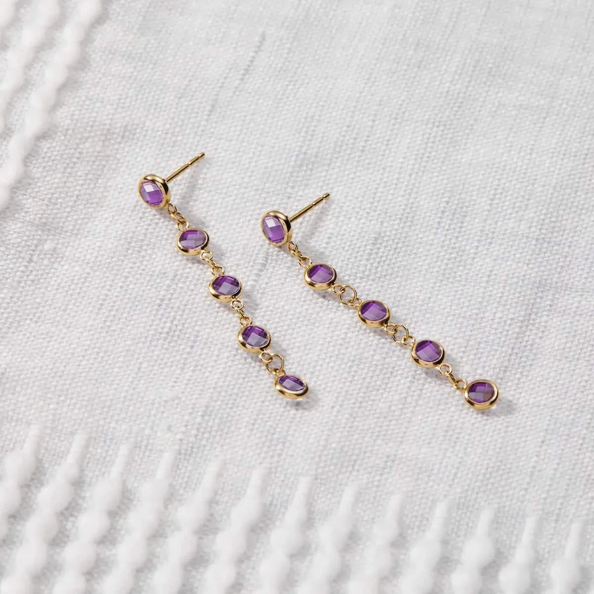 Newport Amethyst Earrings in 14k gold are displayed on fabric, featuring five bezel-set briolette-cut amethysts.