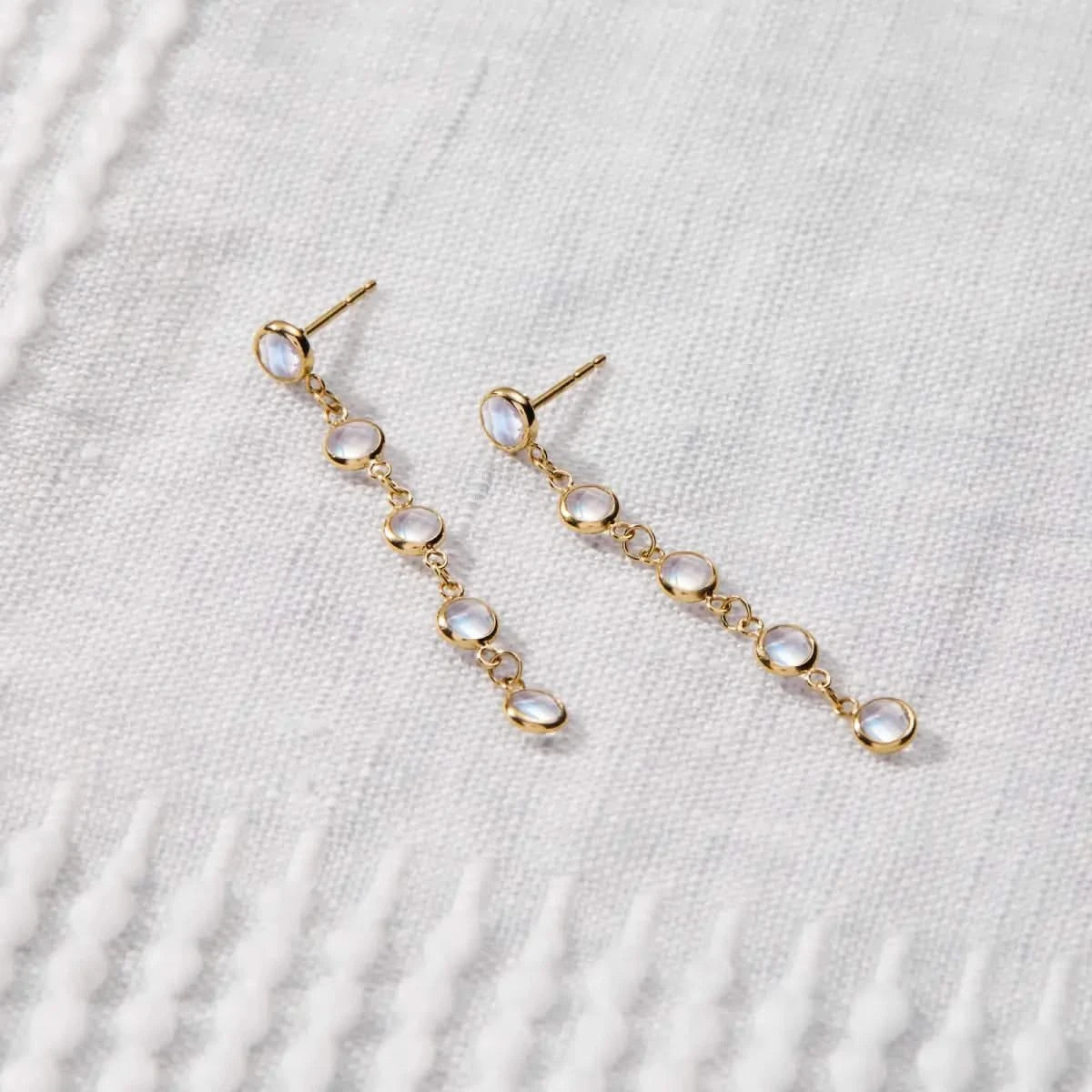 Newport Moonstone Earrings in 14k gold are shown laid flat, highlighting bezel set moonstones in a linear drop design.