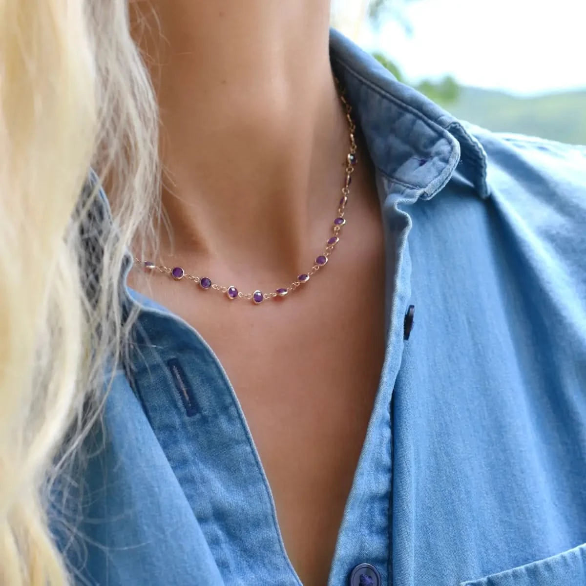 Woman wearing Newport amethyst necklace in 14k gold styled casually outdoors with open shirt collar.