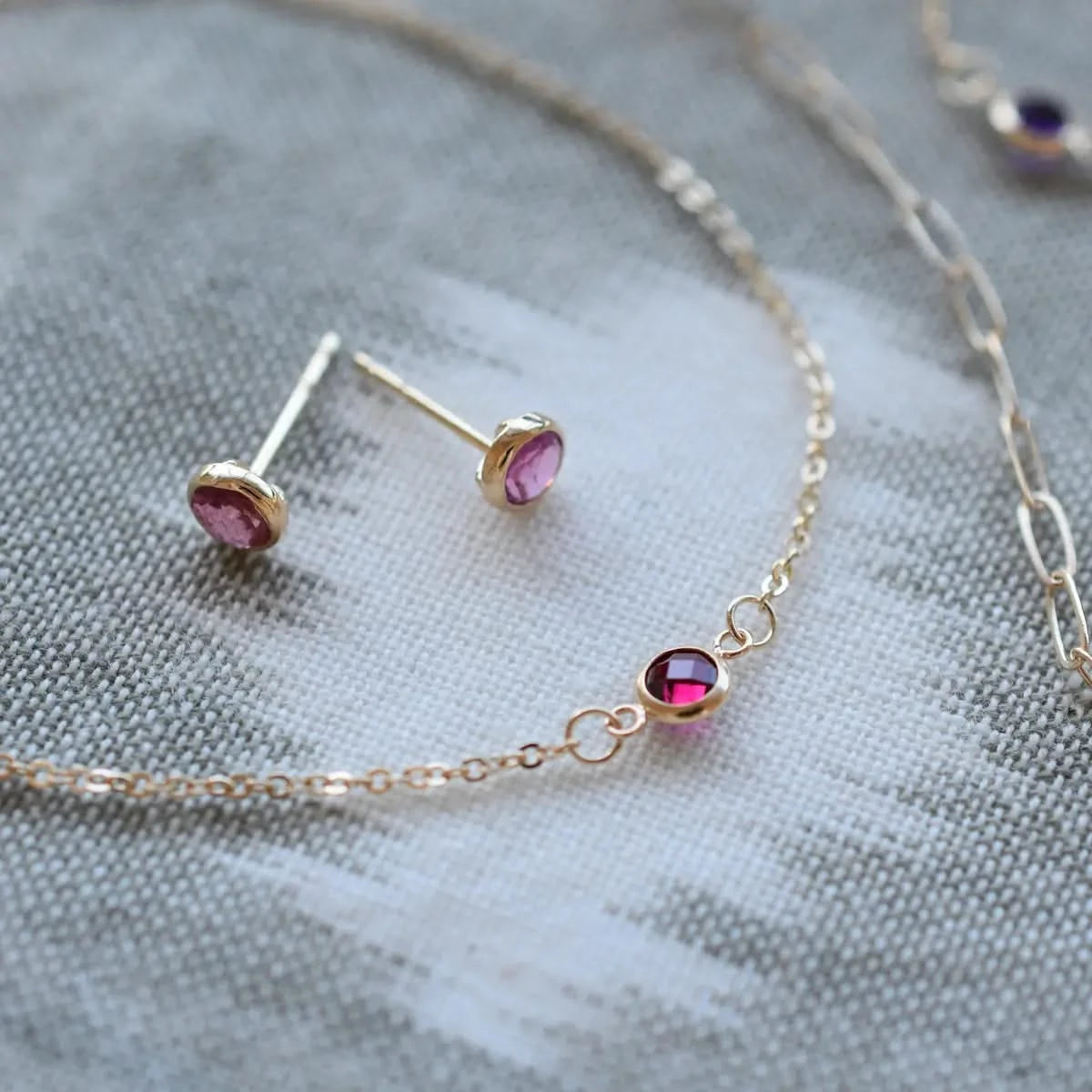 Assorted jewelry, including a pair of Petite Stud Earrings and a Petite Necklace, both featuring 4 mm Pink Sapphires bezel set in 14k yellow gold.