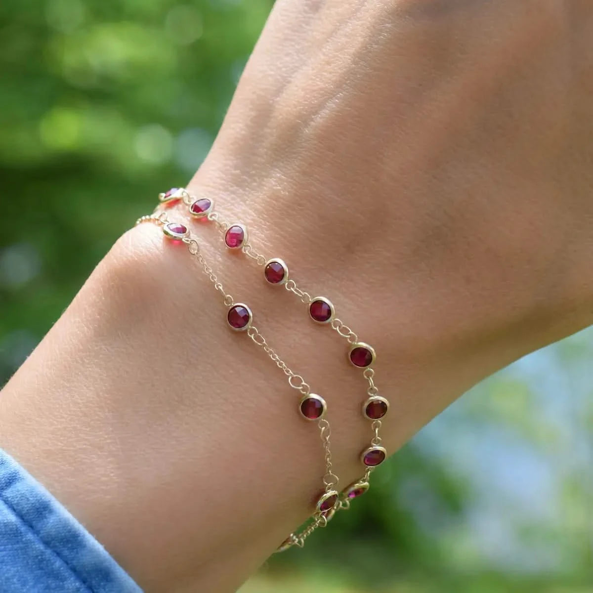 Woman wearing two bracelets including a Newport 14k yellow gold bracelet featuring 4 mm briolette cut bezel set rubies