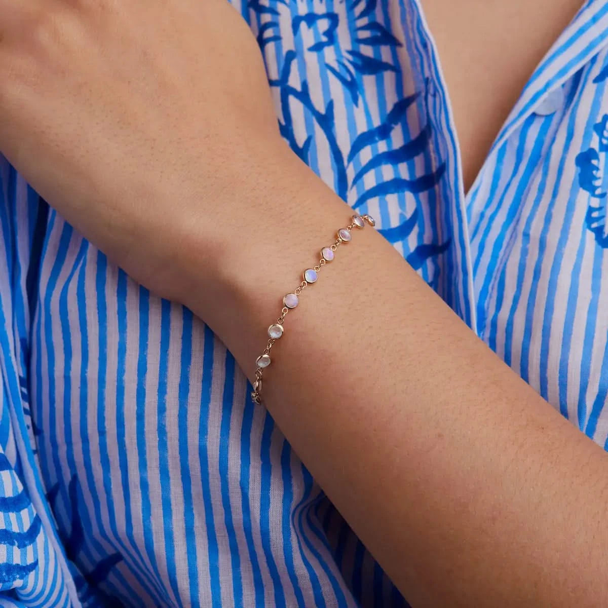 Close-up of Newport Moonstone Bracelet in 14k Gold worn on wrist, featuring round bezel set moonstones against a striped blue and white shirt.