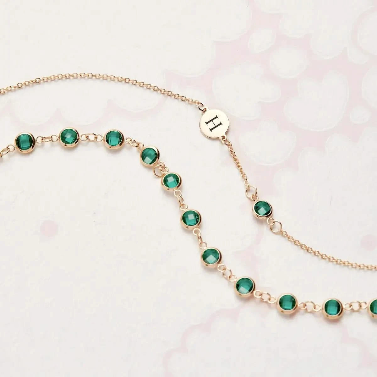 Close-up of the Newport Emerald Chain paired with an initial charm bracelet, showcasing bezel set round emeralds in 14k gold.