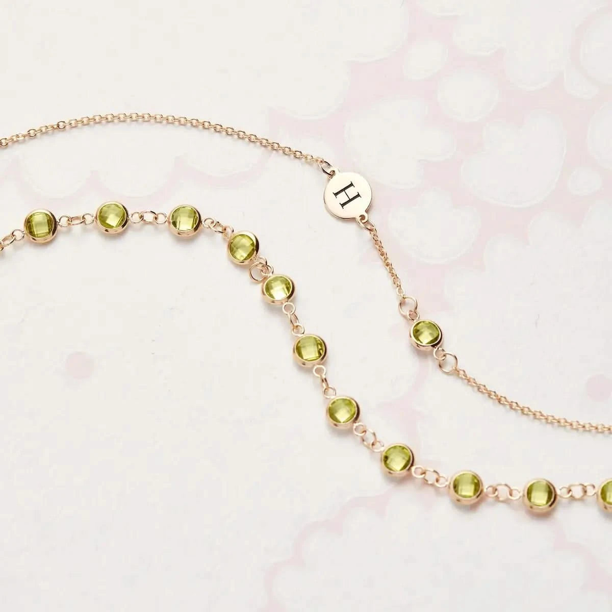 Flatlay of the Newport Peridot Chain in 14k gold, paired with an engraved initial charm and briolette-cut Peridot stones.