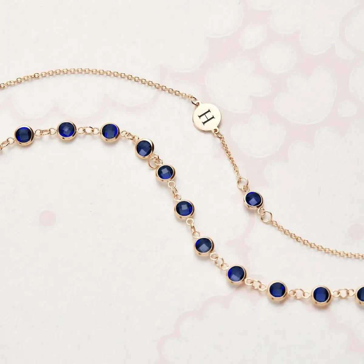 Flatlay of Newport Sapphire Necklace in 14k Gold featuring round bezel set sapphires with engraved “H” tag detail.