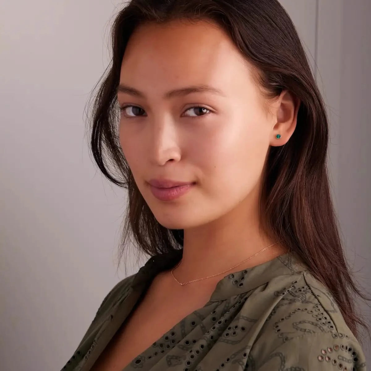 Woman wearing a Petite Stud Earring featuring a 4 mm briolette cut Emerald bezel set in 14k yellow gold