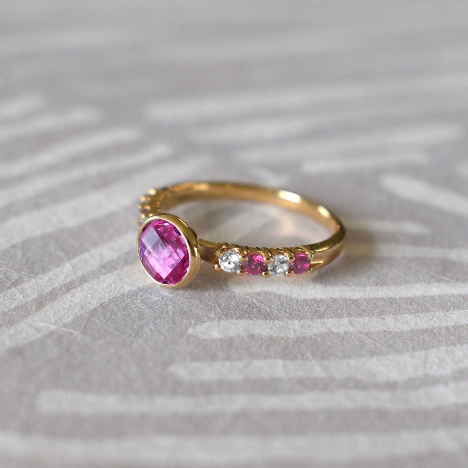 Woman showcasing a 14k gold Rosecliff Grand Ring with a 6 mm briolette-cut Pink Sapphire and eight alternating 2 mm round-cut Diamonds and Pink Sapphires.