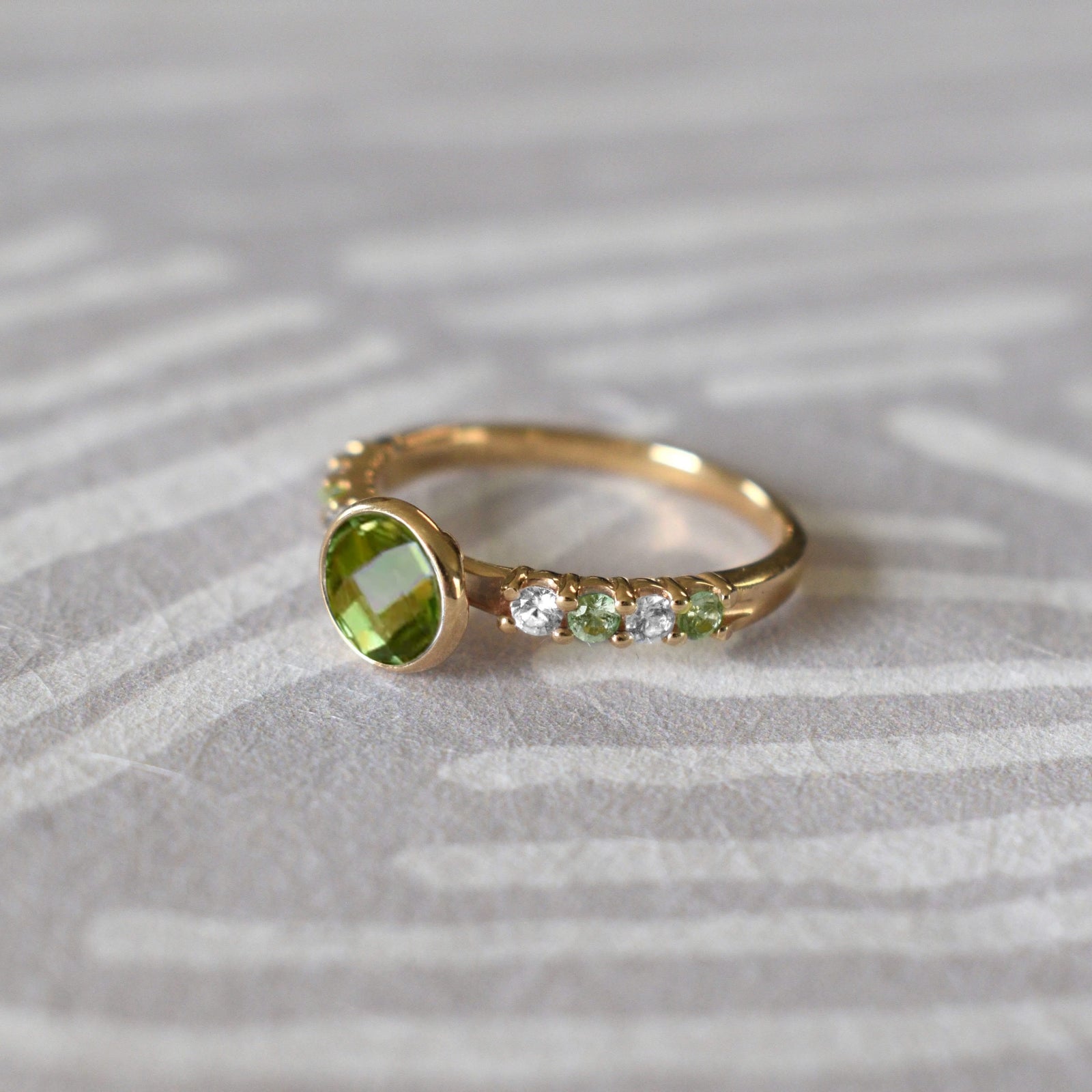 A 14k gold Rosecliff Grand Ring with a 6 mm briolette-cut Peridot and eight 2 mm round-cut alternating Diamonds and Peridots.
