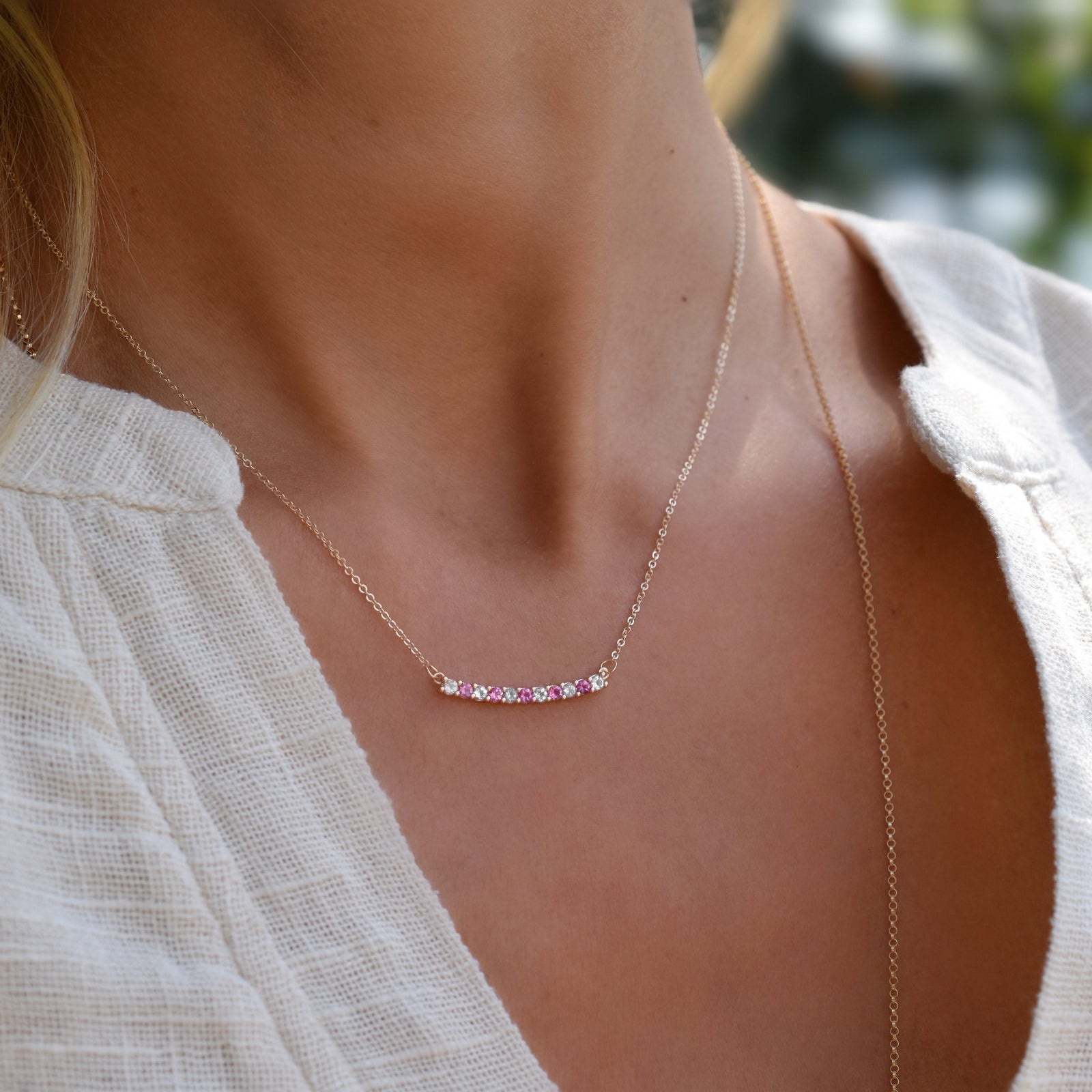 Women wearing a Rosecliff bar necklace with eleven alternating 2 mm pink sapphires & diamonds prong set in 14k gold