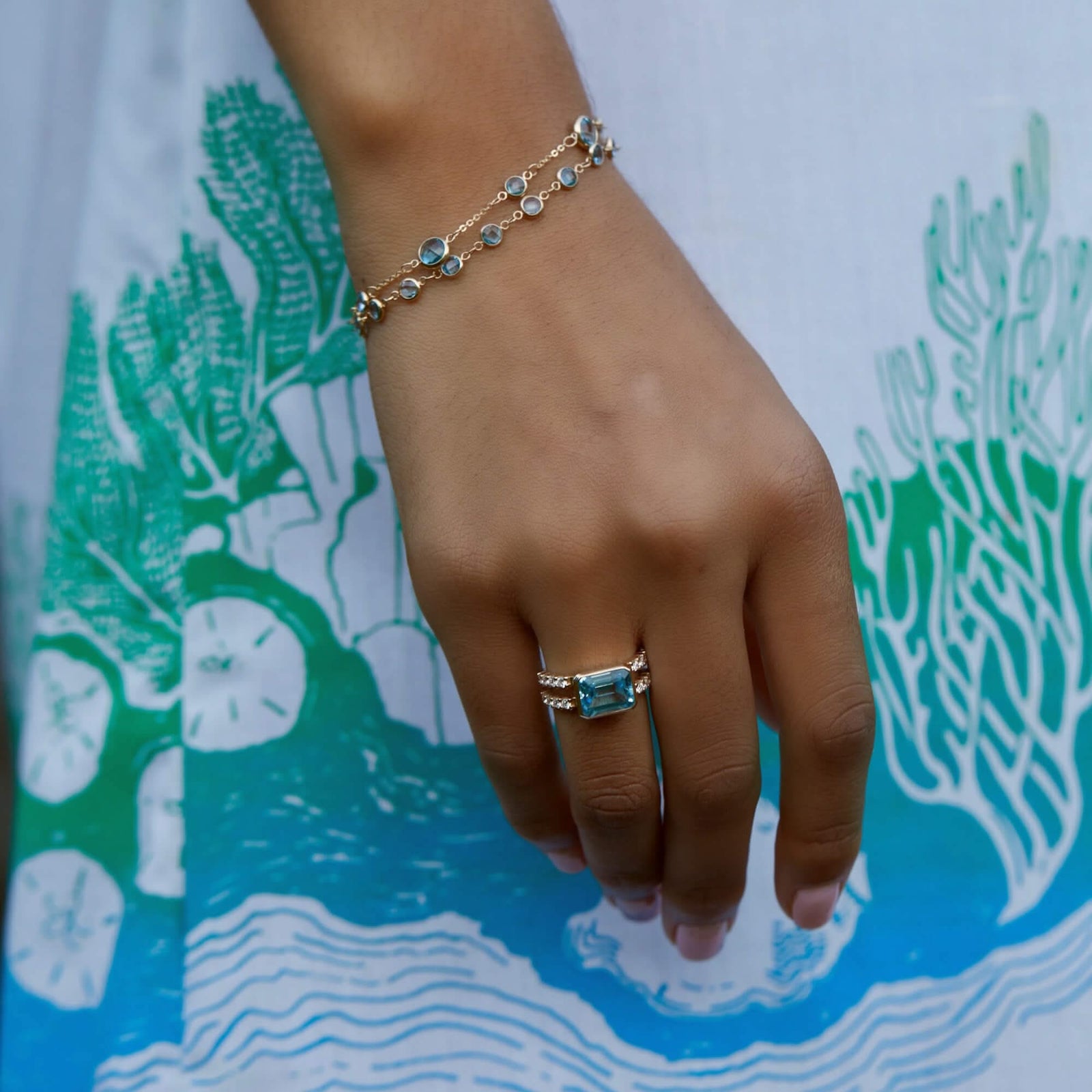 Woman adorned with a 14k yellow gold Warren Horizontal Nantucket Blue Topaz Ring with Diamonds, showcasing an 8 x 10mm Nantucket Blue Topaz and 16 prong-set diamonds.