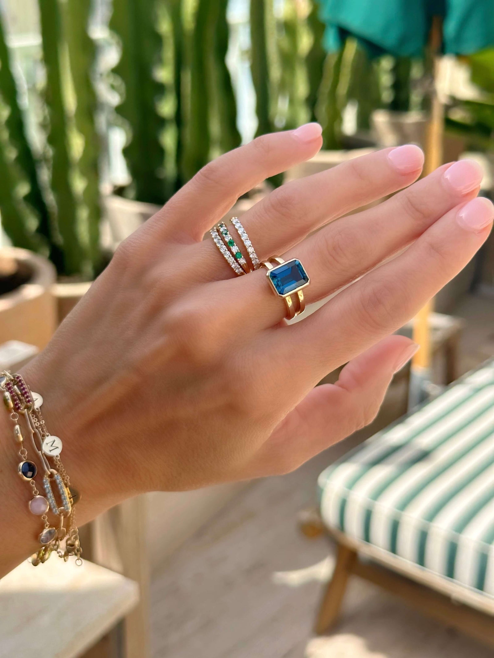Woman adorned with assorted Haverhill 14k gold rings, including a Warren Vertical Ring, showcasing one 10 x 8 mm emerald cut, bezel set Atlantic Blue Topaz in 14k Gold.