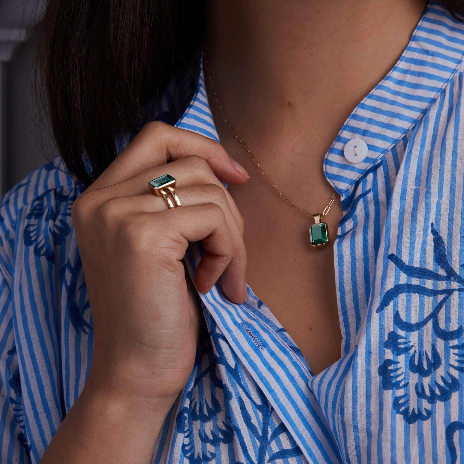Woman showcasing a 14k yellow gold Warren Emerald Pendant and matching Vertical Emerald Ring, featuring one 10 x 8 mm emerald cut, bezel set Emerald.