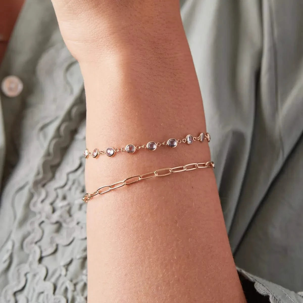 Close-up of a wrist wearing a Newport Aquamarine Bracelet in 14k gold layered with a gold paperclip chain bracelet.