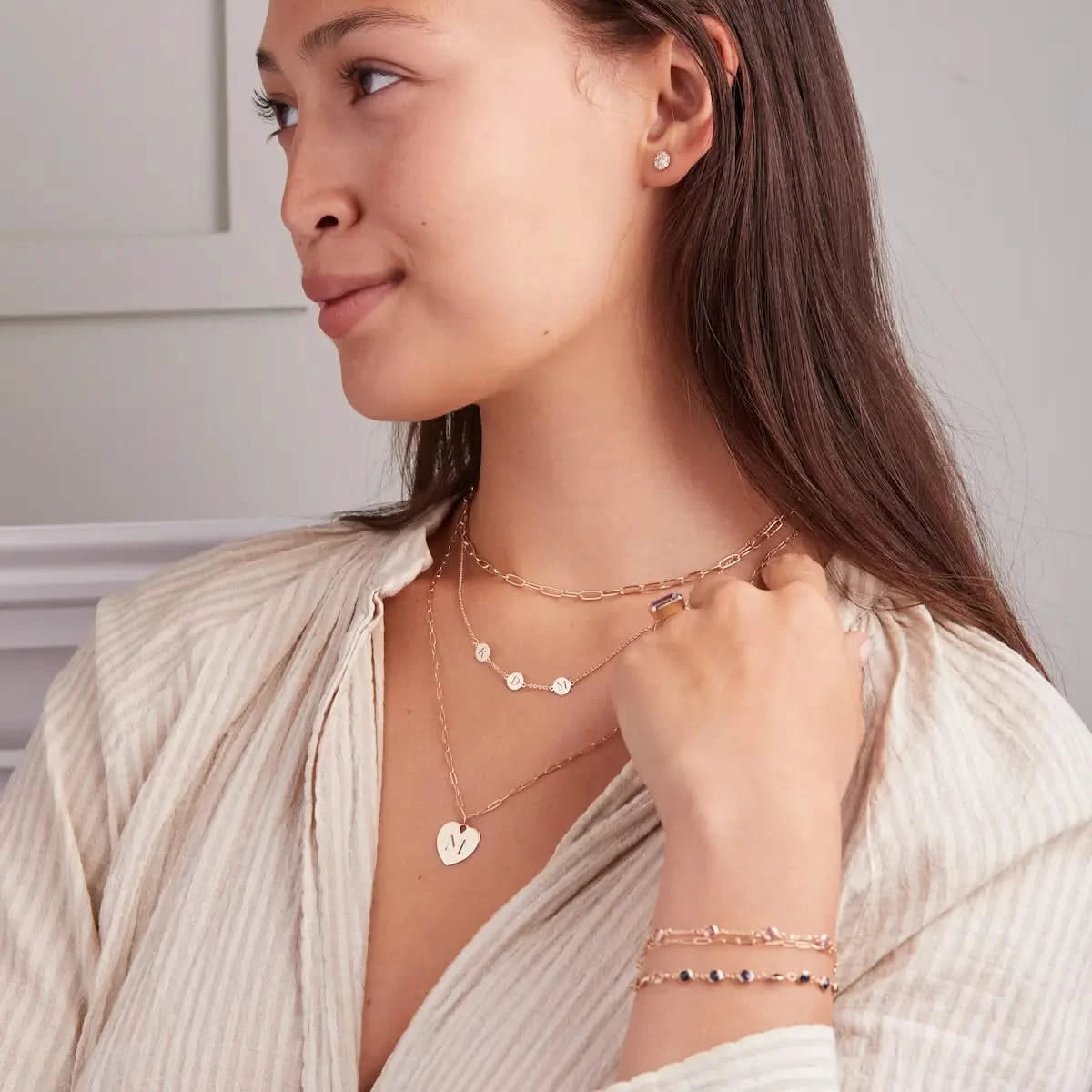 Woman wearing layered necklaces including engraved “M” Small Flat Heart Pendant in 14k gold with Adelaide Mini chain.