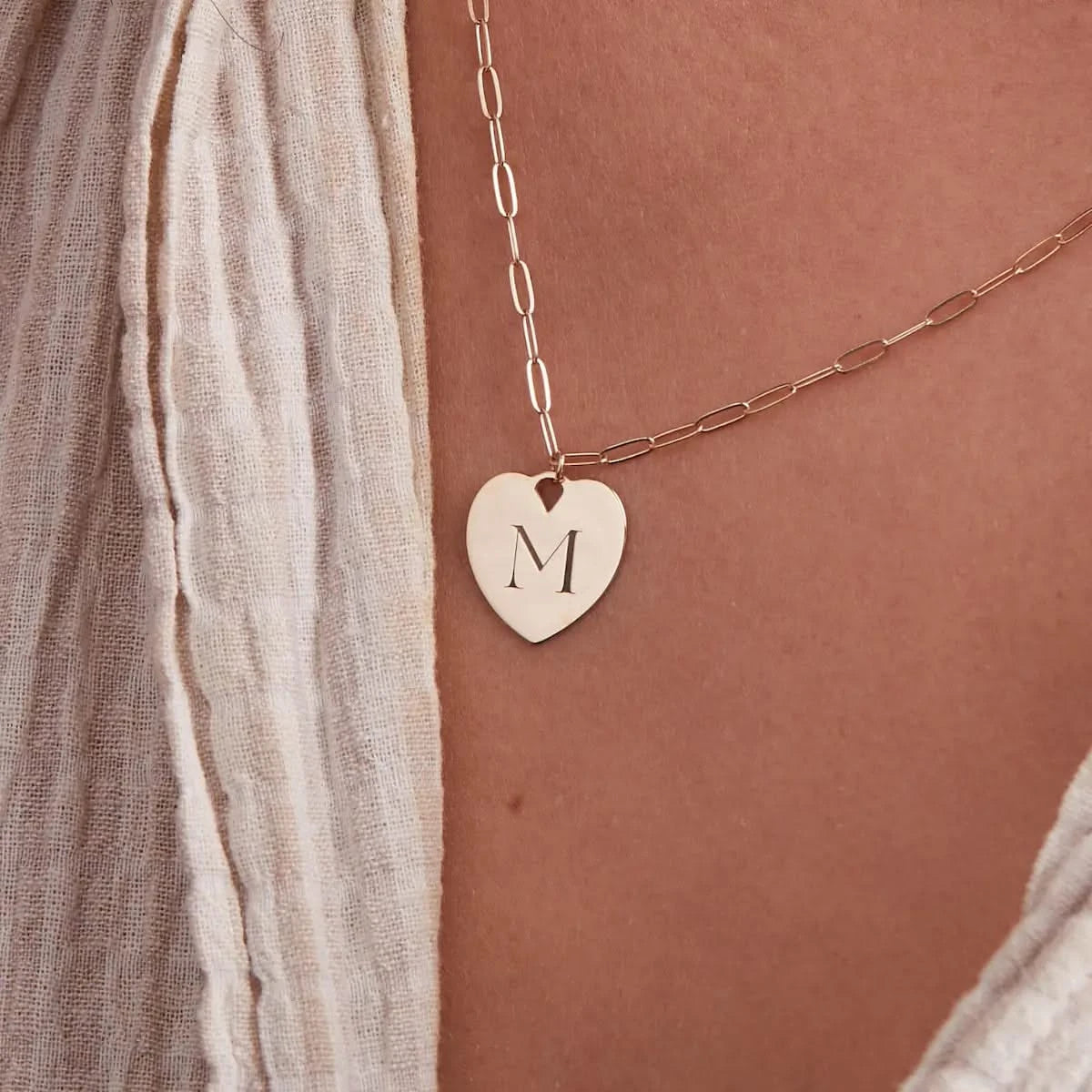 Close-up of the Small Engravable Flat Heart Pendant in 14k gold on an Adelaide Mini Chain, engraved with the initial "M".