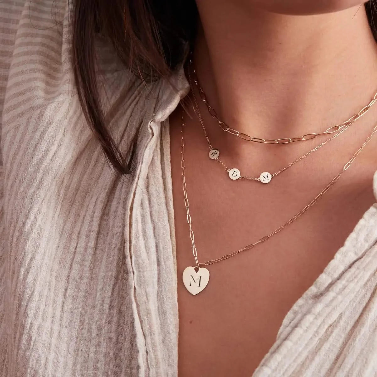 Layered look featuring the Small Engravable Flat Heart Pendant in 14k gold with the initial "M" and a horizontal three-initial necklace above.