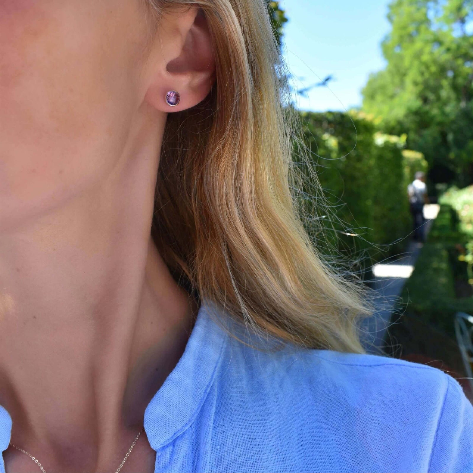 Woman adorned with a pair of Grand Birthstone Stud Earrings in 14k Gold featuring one 6 mm briolette cut, bezel set Amethyst.
