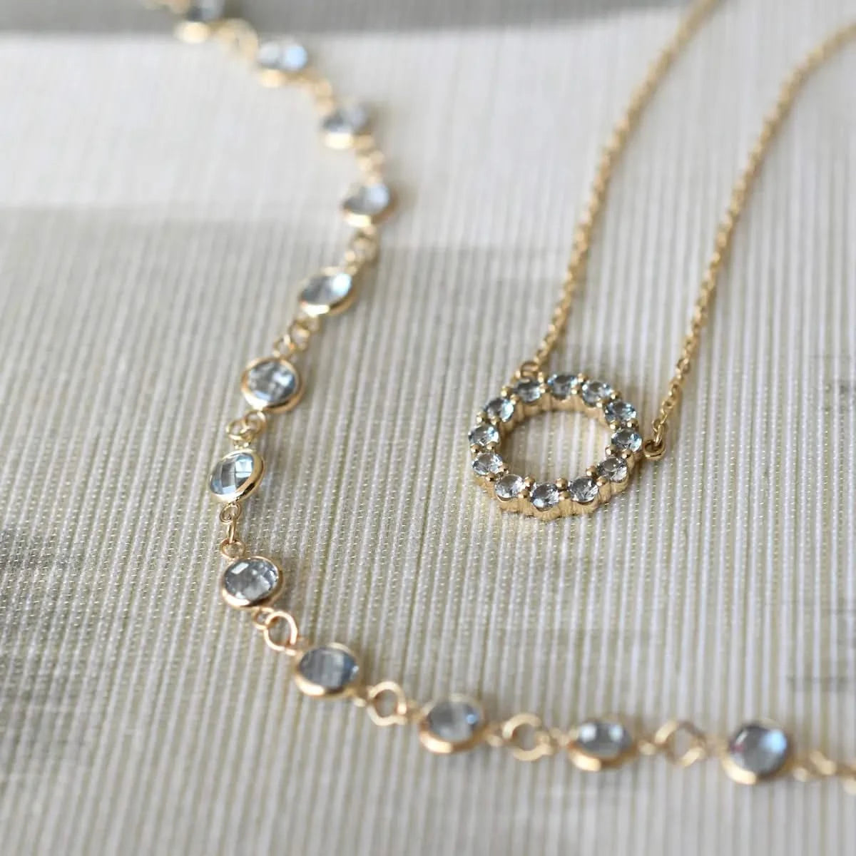 Flatlay of Newport Aquamarine necklace with yellow gold Rosecliff Small Circle necklace on fabric.