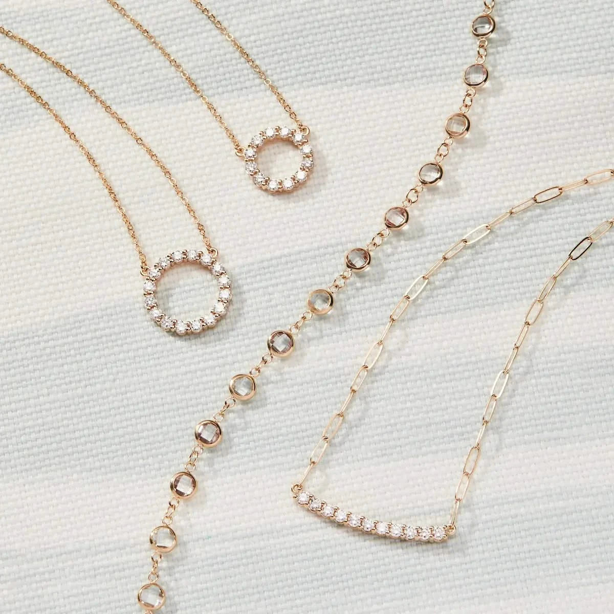 Flatlay of the Newport White Topaz Necklace paired with two pavé diamond circle pendants and a gold bar necklace on a soft white background.