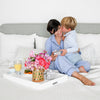 Mother and son on bed. Son kisses mother's cheek and gives her a Haverhill jewelry box for Mother's Day.