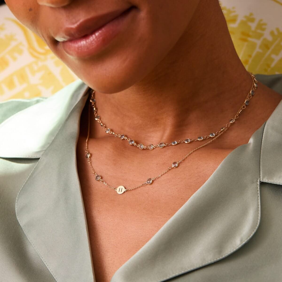 Close-up of layered Nantucket Blue Topaz necklaces in 14k gold, one featuring a custom engraved initial charm.