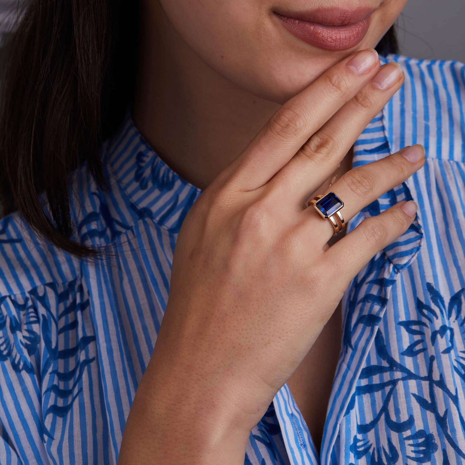 Woman adorned with a 14k yellow gold Warren Vertical Sapphire Ring, showcasing one 10 x 8 mm emerald cut, bezel set Sapphire.