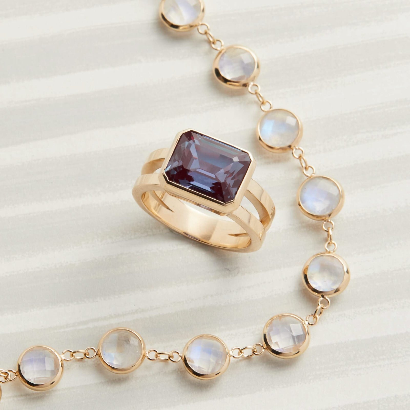 Assorted jewelry featuring a 14k gold Warren ring with an emerald-cut Alexandrite, paired with a moonstone necklace.
