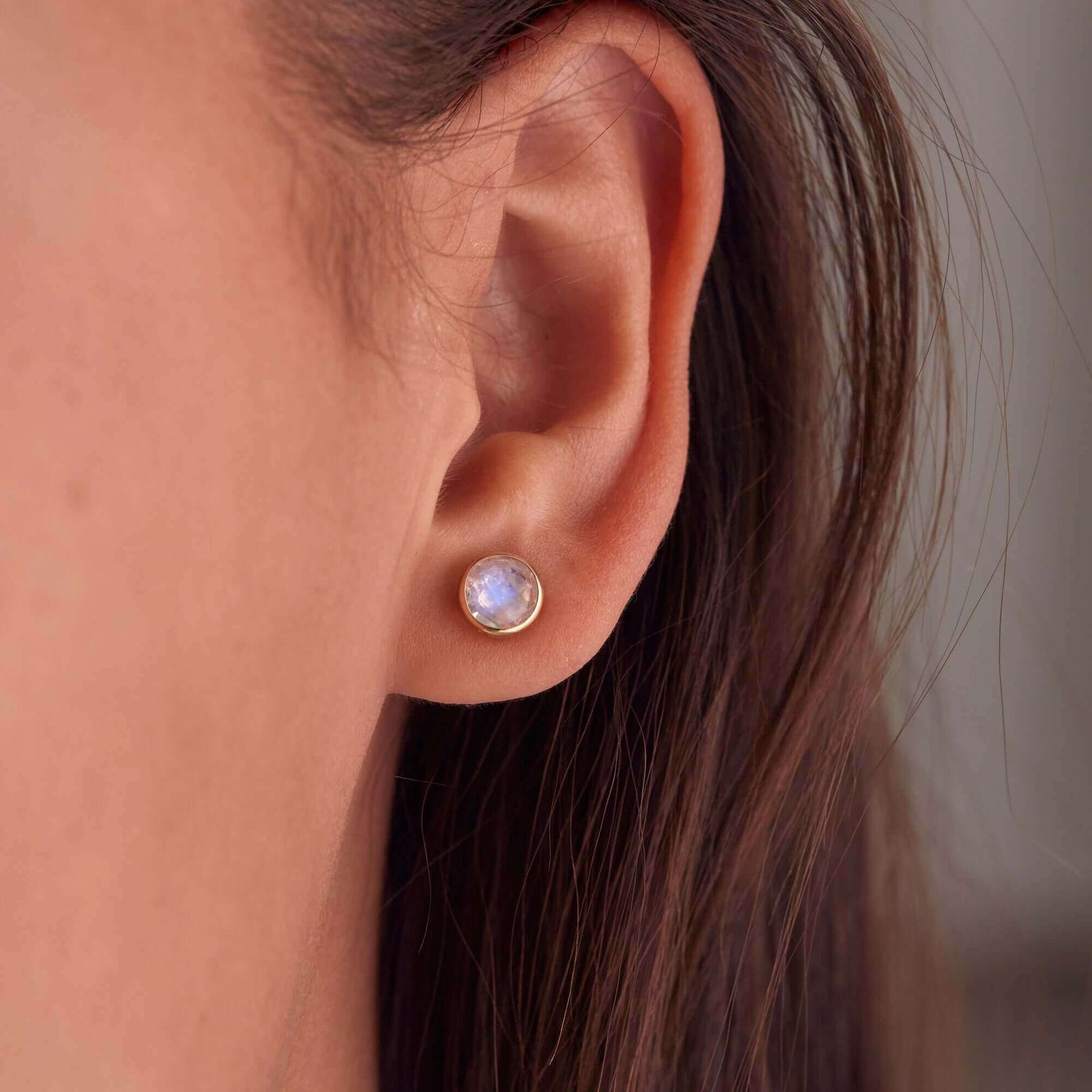 Woman showcasing a 14k yellow gold Grand stud earring featuring one 6 mm briolette cut bezel set moonstone